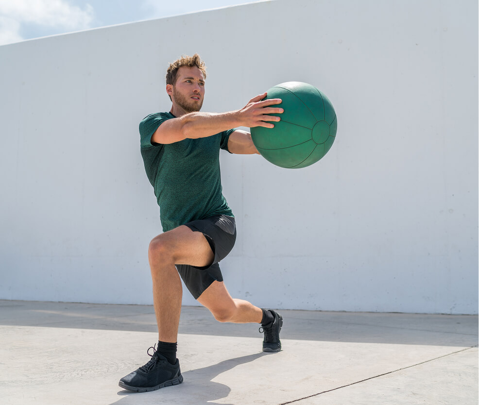 Man exercising outdoors with weight ball.